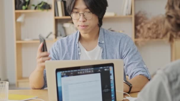 Sorridente Giovane Uomo Asiatico Parlando Smartphone Guardando Lontano Mentre Seduto — Video Stock