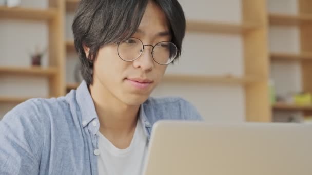 Calma Jovem Asiático Homem Óculos Usando Computador Portátil Enquanto Sentado — Vídeo de Stock