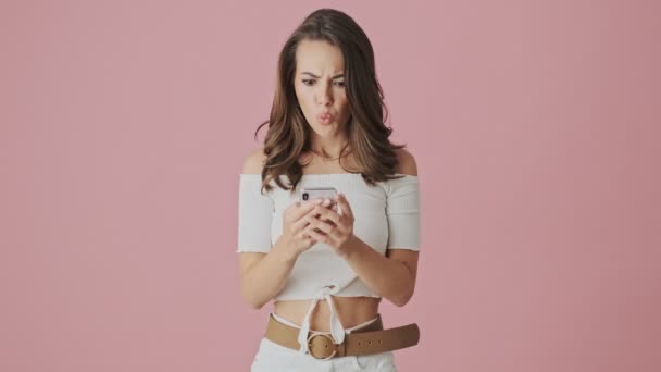 Злая Молодая Женщина Печатает Своем Смартфоне Находясь Изоляции Розовом Фоне — стоковое видео
