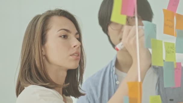 Dos Jóvenes Colegas Enfocados Escribiendo Algo Pegatinas Coloridas Pegadas Pared — Vídeos de Stock