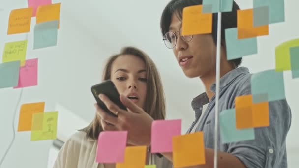 Two Calm Young Colleagues Using Smartphone While Standing Glass Wall — Stock Video