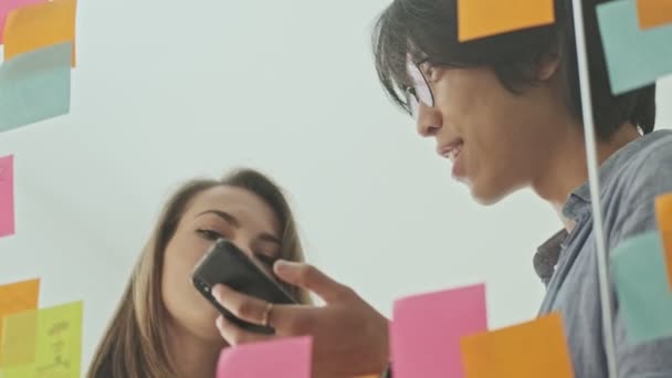 Dos Jóvenes Colegas Sonrientes Usando Teléfono Inteligente Hablando Algo Mientras — Vídeos de Stock