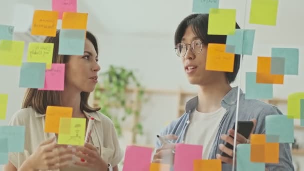 Two Happy Young Colleagues Talking Something While Standing Glass Wall — Stock Video