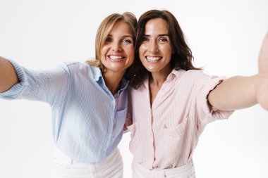 Beyaz arka planda izole edilmiş selfie çekilirken sarılan iki güzel kadının görüntüsü.