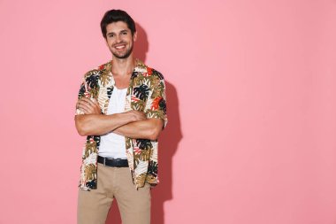 Pembe arka planda izole edilmiş, gülümseyen ve poz veren parlak tişörtlü neşeli genç adamın portresi.