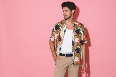 Pembe arka planda tek başına poz veren ve yan bakan kendine güvenen genç bir adamın portresi.