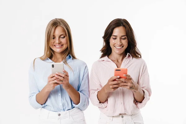 笑顔と白い背景に隔離された携帯電話を使用して幸せな魅力的な2人の女性のイメージ — ストック写真