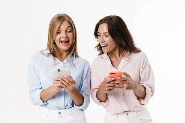 Imagem Duas Mulheres Lindas Excitadas Usando Telefones Celulares Isolados Sobre — Fotografia de Stock