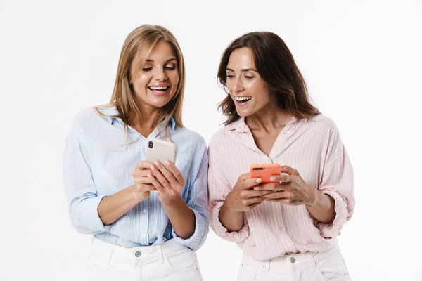 白い背景に隔離された携帯電話を使用して美しい興奮した2人の女性のイメージ — ストック写真