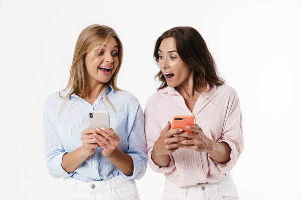Изображение Красивых Возбужденных Двух Женщин Использующих Мобильные Телефоны Белом Фоне — стоковое фото