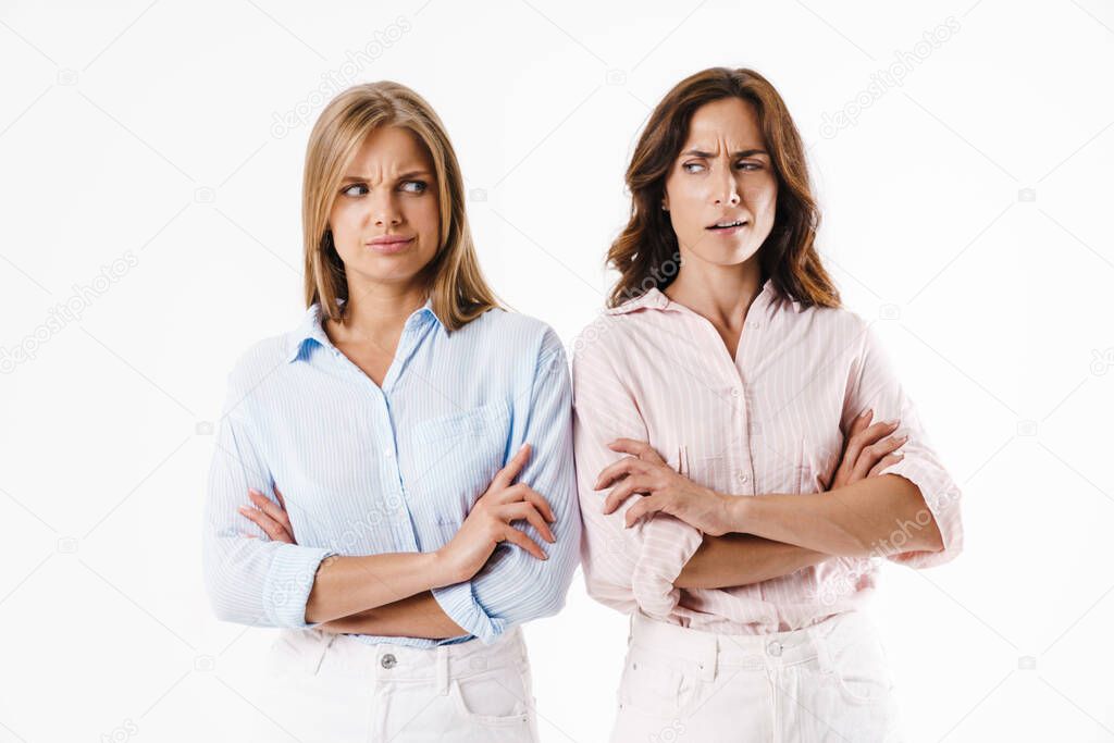 Image of resentful two women looking at each other while posing with hands crossed isolated over white background