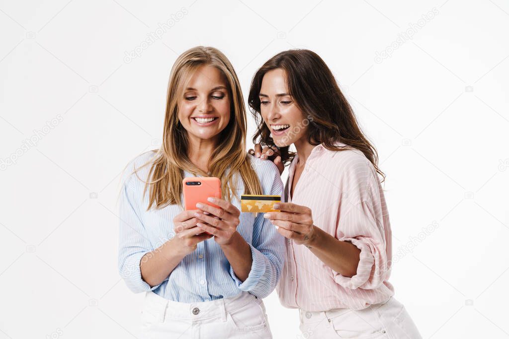 Image of charming cheerful two women using mobile phone and holding credit card isolated over white background