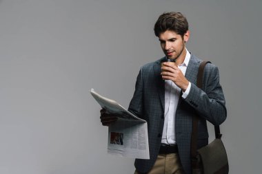 Gri duvarda izole edilmiş gazete okurken kahve içen genç işadamının fotoğrafı