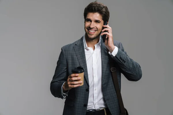 照片中 一个微笑的商人一边喝着咖啡 一边隔着灰墙一边用手机聊天 — 图库照片
