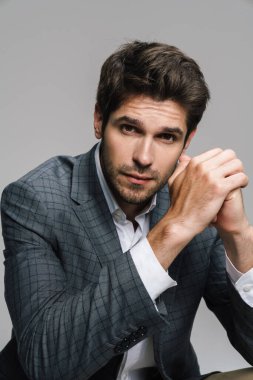 Ceketli saygıdeğer iş adamının fotoğrafı gri duvarın üzerinde izole bir şekilde oturuyor ve kameraya bakıyor.