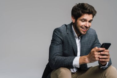 Gri duvarda tek başına otururken cep telefonu kullanan saygıdeğer gülen iş adamının fotoğrafı.