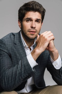 Ceketli saygıdeğer iş adamının fotoğrafı gri duvarın üzerinde izole bir şekilde oturuyor ve kameraya bakıyor.