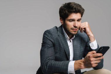 Gri duvarda tek başına otururken cep telefonu kullanan saygıdeğer, kendine güvenen bir iş adamının fotoğrafı.