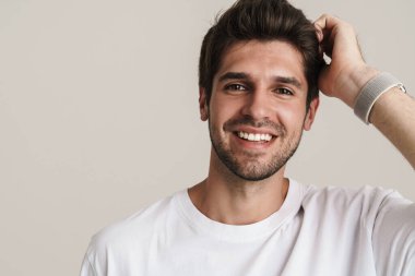 Temel tişörtlü neşeli genç adamın portresi gülümseyen ve beyaz arka planda izole edilmiş kameraya bakan