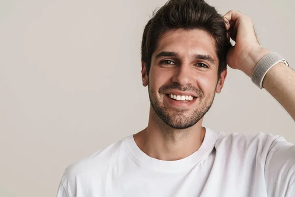 Portrait of joyful young man in basic t-shirt smiling and looking at camera isolated over white background