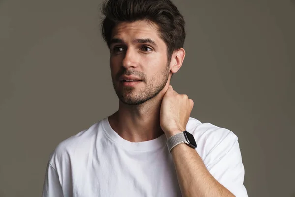 Portrait of confident young man in basic t-shirt posing and looking aside isolated over grey background