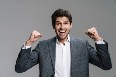 Heyecanlı yakışıklı iş adamının gri duvarda izole bir şekilde kameraya yaptığı güzel jestin fotoğrafı.