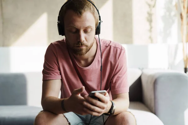 Foto Joven Pelirrojo Con Barba Usando Teléfono Móvil Auriculares Mientras —  Fotos de Stock