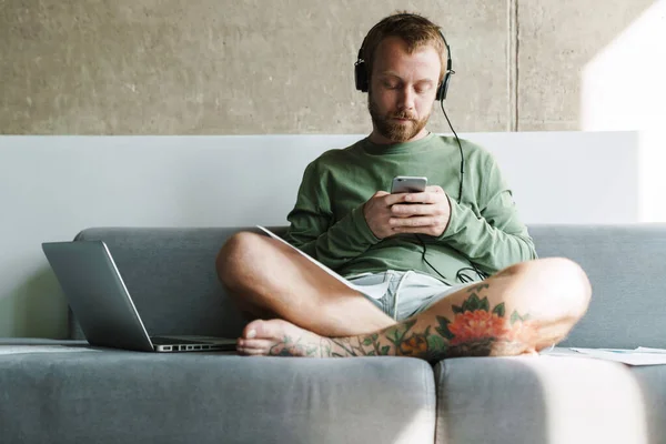 Foto Joven Centrado Uso Teléfono Móvil Auriculares Mientras Trabaja Con —  Fotos de Stock