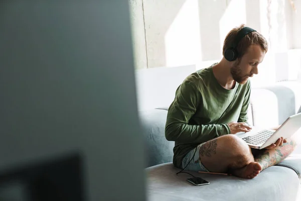 Foto Hombre Joven Concentrado Usando Teléfono Móvil Auriculares Mientras Trabaja — Foto de Stock