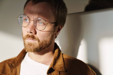 Gözlüklü, poz veren ve içeri bakan genç adamın yakın plan fotoğrafı.