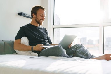 Parlak odada dizüstü bilgisayarla çalışırken gülümseyen beyaz adamın mutlu bir fotoğrafı.