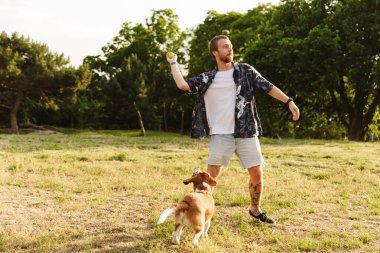 Kafkas sakallı genç bir adamın yaz parkında yürürken av köpeğiyle oynaması.