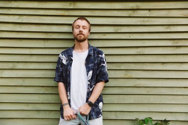 Kafkasyalı sakallı bir gencin ahşap duvarın yanında durup sana gülümseyen ve bakan görüntüsü.