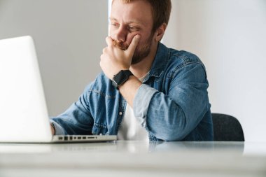 Kırmızı sakallı, düşüncelere dalmış yakışıklı bir adamın fotoğrafı.