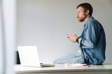İçerideki masada otururken cep telefonu ve laptop kullanan kızıl sakallı yakışıklı bir adamın fotoğrafı.