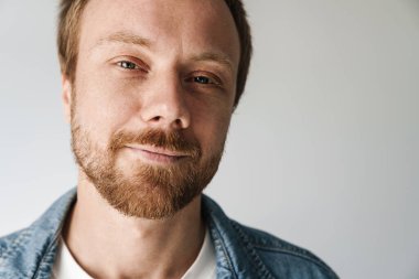 Gri arka planda izole edilmiş, kızıl saçlı, poz veren ve gülümseyen neşeli genç adamın fotoğrafı.