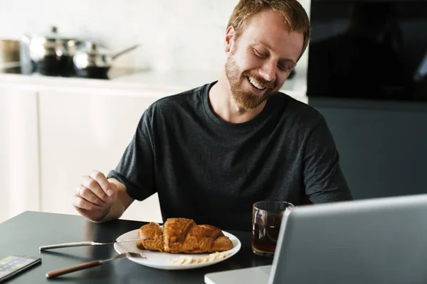 Foto Jovem Rindo Com Barba Usando Laptop Enquanto Toma Café — Fotografia de Stock