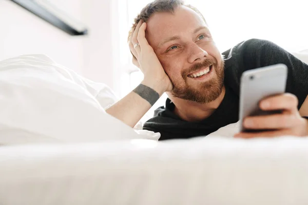 Foto Hombre Barbudo Sonriente Usando Teléfono Móvil Mientras Está Acostado — Foto de Stock