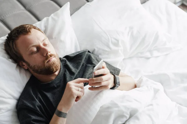 Foto Homem Barbudo Focado Usando Telefone Celular Enquanto Estava Deitado — Fotografia de Stock