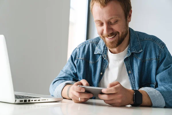 Fénykép Mosolygós Jóképű Férfi Játszik Online Játék Mobiltelefon Miközben Dolgozik — Stock Fotó