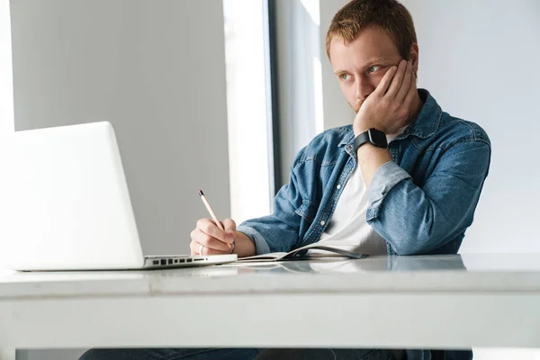 Foto Pensar Homem Bonito Escrevendo Notas Enquanto Trabalhava Com Laptop — Fotografia de Stock