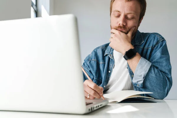 Foto Pensar Homem Bonito Escrevendo Notas Enquanto Trabalhava Com Laptop — Fotografia de Stock