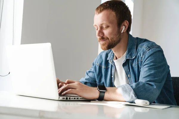 Foto Del Hombre Jengibre Satisfecho Usando Auriculares Inalámbricos Mientras Trabaja — Foto de Stock