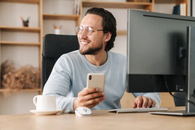 Ofiste bilgisayarla çalışırken gözlük takan gülümseyen programcı görüntüsü