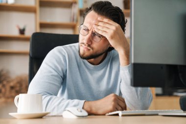 Ofiste bilgisayarla çalışan, gözlüklü, kara kara düşünen sakallı programcı.