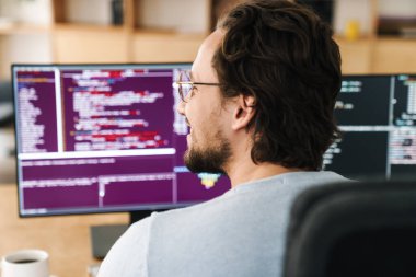 Ofisteki bilgisayarlarla çalışan, gözlüklü, tıraşsız, memnun programcının resmi