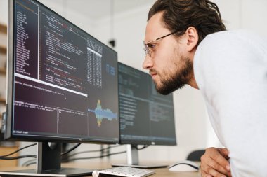 Ofiste bilgisayarlarla çalışan, gözlük takan konsantre olmamış programcı görüntüsü