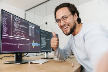 Ofisteki bilgisayarlarla çalışırken gülümseyen traşsız programcı görüntüsü