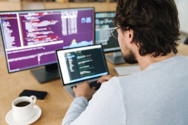 Ofisteki bilgisayarlarla çalışan gözlüklü beyaz programcı görüntüsü
