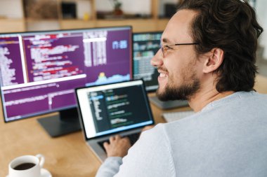 Ofiste bilgisayarlarla çalışan gözlüklü neşeli beyaz programcı görüntüsü